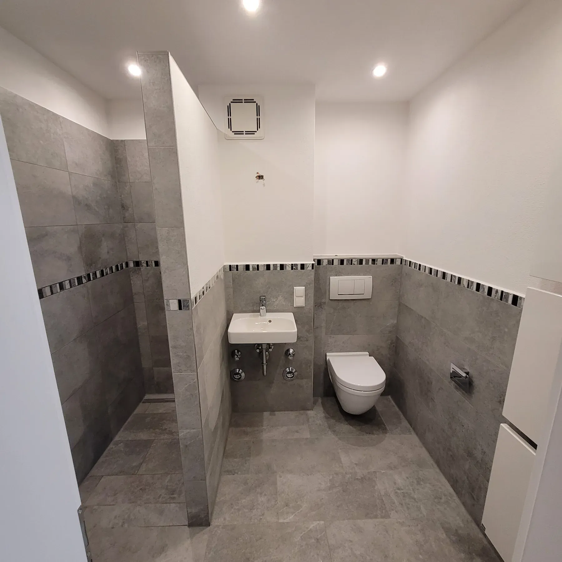 Fertiggestelltes Gaestebad mit grauen Fliesen, Dusche und Wand-WC
